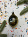 a shiny, metallic ornament with a textured surface, surrounded by colorful confetti and a sprig of greenery.