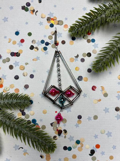 a decorative metal earring with a geometric design, surrounded by confetti and pine branches.