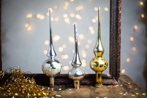 Three decorative ornaments with unique shapes and sizes are displayed on a wooden surface, with a blurred background of lights.