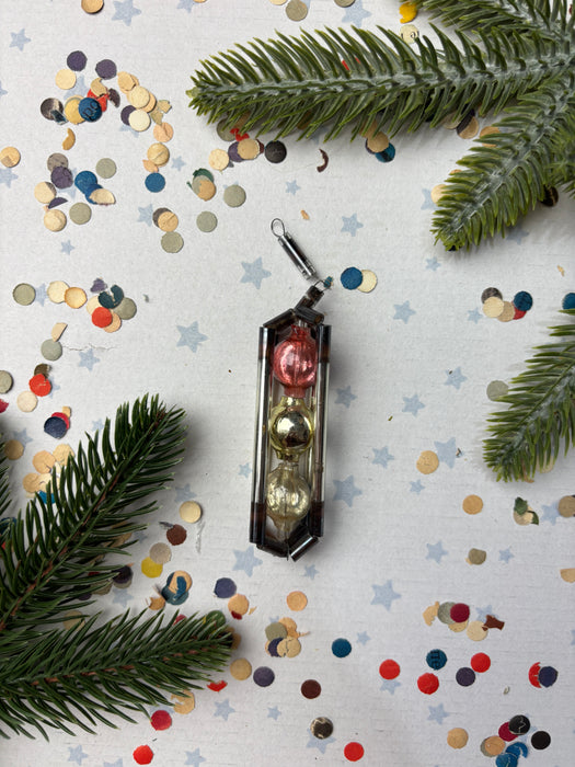 a Christmas ornament with three glass balls, surrounded by confetti and pine branches.