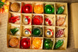 A box filled with various Christmas ornaments, including red, green, and yellow balls, as well as other ornaments in different shapes and sizes.