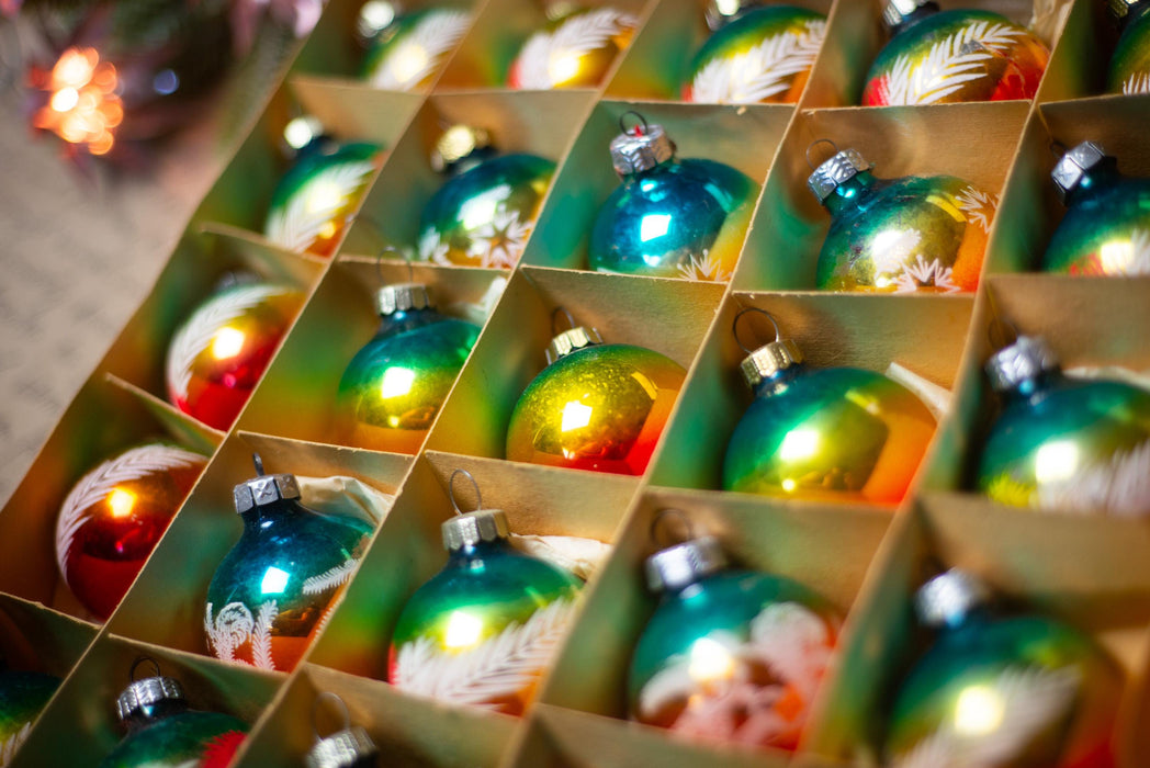 A close-up view of a collection of colorful Christmas ornaments arranged in a grid-like pattern, with a blurred background suggesting a festive setting.