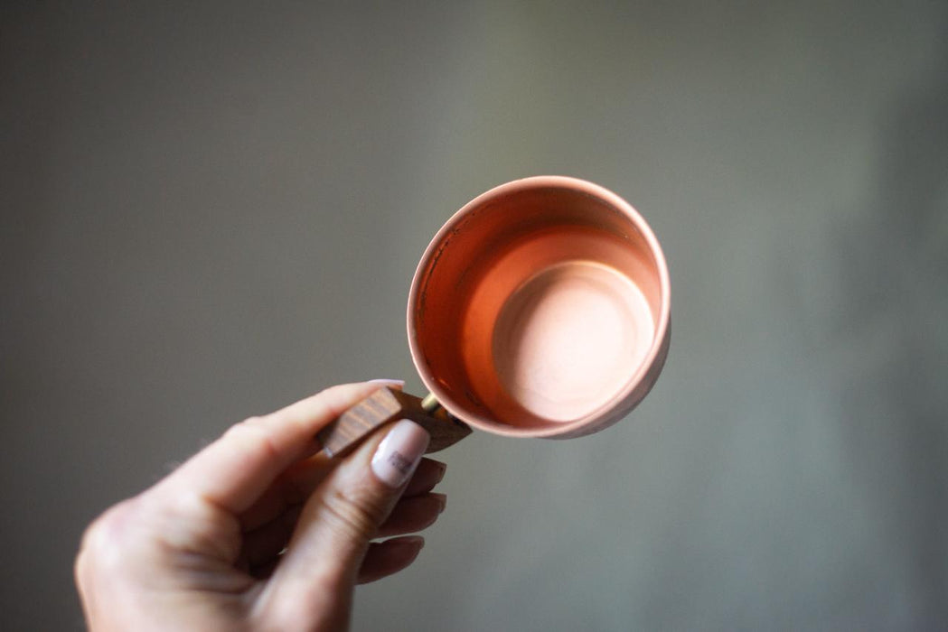 A hand holding a copper-colored mug against a gray background.
