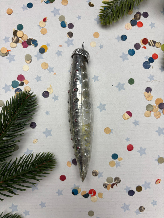a silver ornament with a pointed end, surrounded by colorful confetti and pine branches.