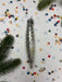 a silver ornament with a pointed end, surrounded by colorful confetti and pine branches.