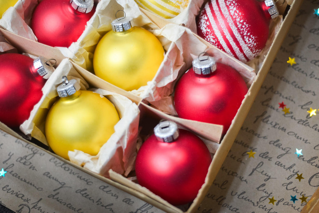 A box filled with Christmas ornaments, including red and yellow balls, placed on a surface with some scattered stars.