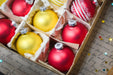 A box filled with Christmas ornaments, including red and yellow balls, placed on a surface with some scattered stars.