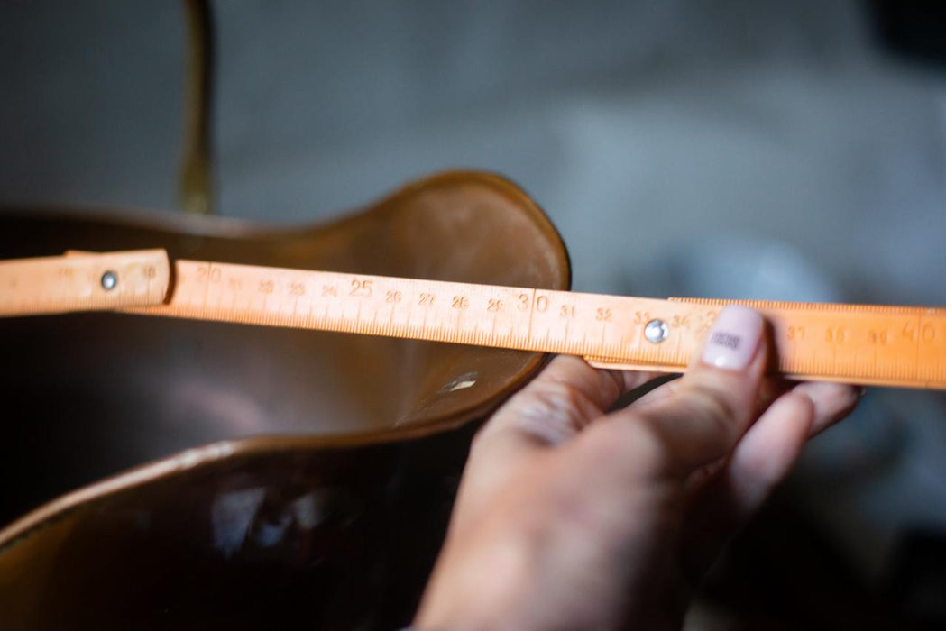A person's hand is holding a wooden ruler with measurements on it, which is placed on a leather surface.