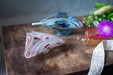 a wooden table with two glass ashtrays, one with a red and white striped design and the other with a blue and white striped design. There is also a book and a purple flower on the table.