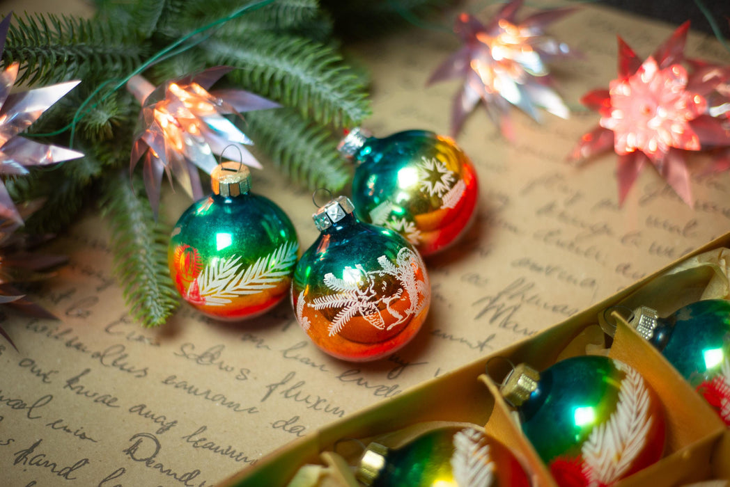 a close-up of Christmas ornaments with a festive background, including greenery and twinkling lights.