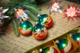 a close-up of Christmas ornaments with a festive background, including greenery and twinkling lights.