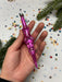 A hand holding a pink ornament against a background of confetti and pine branches.