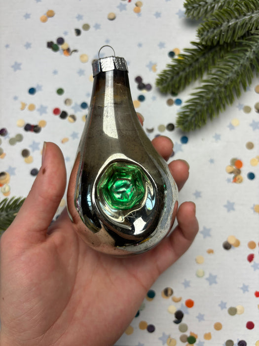 A hand holding a shiny, metallic ornament with a green gem in the center, surrounded by colorful confetti.
