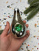 A hand holding a shiny, metallic ornament with a green gem in the center, surrounded by colorful confetti.