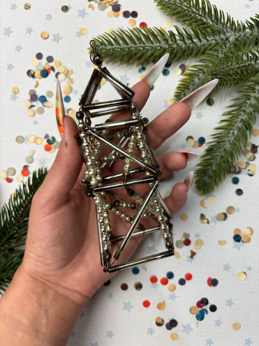 A hand holding a metallic wire sculpture with beads attached, surrounded by confetti and greenery.