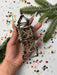 A hand holding a metallic wire sculpture with beads attached, surrounded by confetti and greenery.