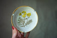 A hand holding a white plate with a yellow floral design on it.