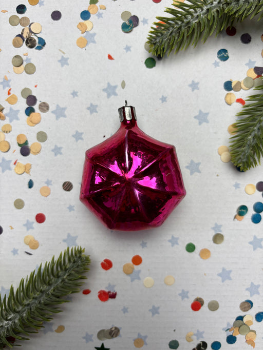 A pink, shiny ornament is surrounded by confetti and pine branches on a white background.