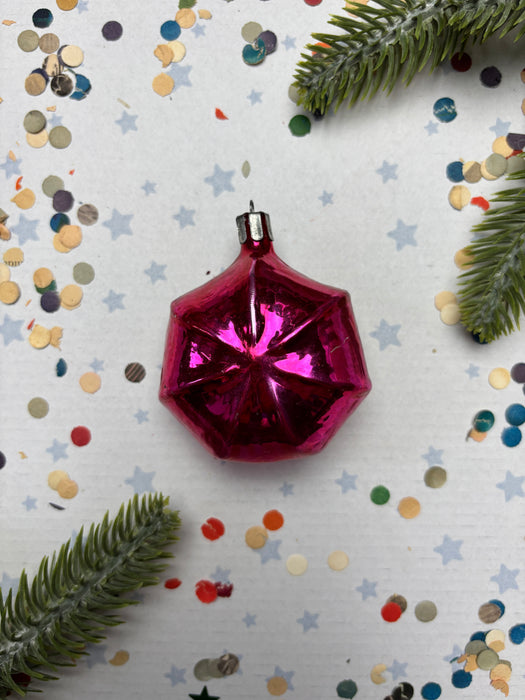 A pink, shiny ornament is surrounded by confetti and pine branches on a white background.