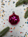 A pink, shiny ornament is surrounded by confetti and pine branches on a white background.