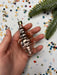 A hand holding a small, shiny, pink ornament against a background of colorful confetti and a pine branch.