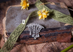 a brooch with a diamond-like design, a green lace ribbon, and a yellow flower on a wooden surface.