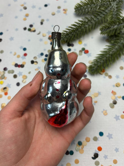 A hand holding a shiny silver ornament with red accents, surrounded by colorful confetti on a festive background.