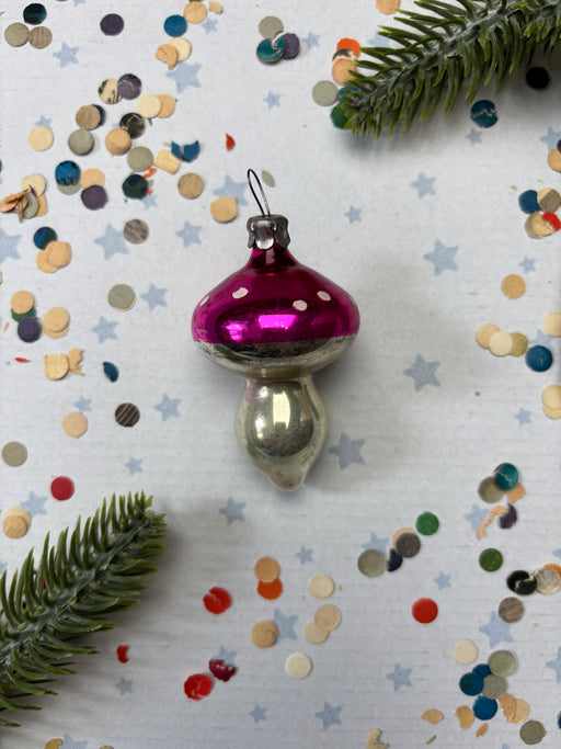 a pink ornament with white polka dots, surrounded by scattered confetti and a sprig of greenery.
