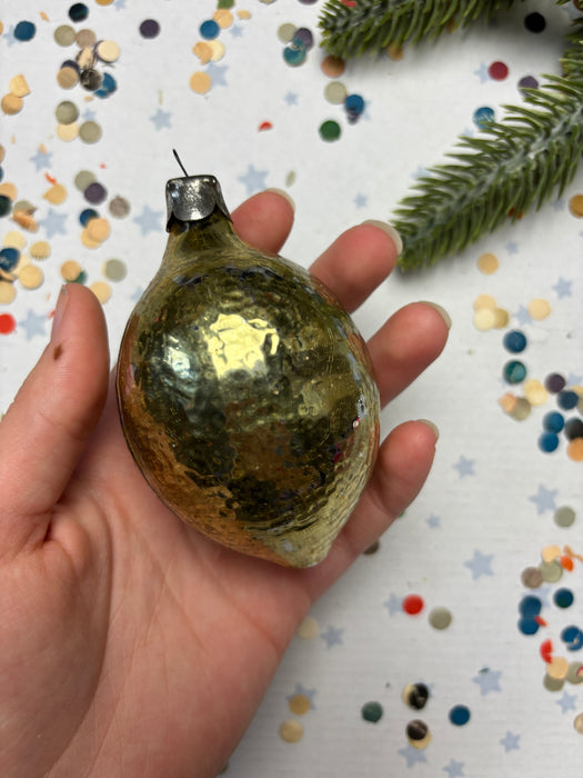 A hand holding a shiny gold ornament against a background of colorful confetti and a small green plant.
