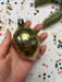A hand holding a shiny gold ornament against a background of colorful confetti and a small green plant.