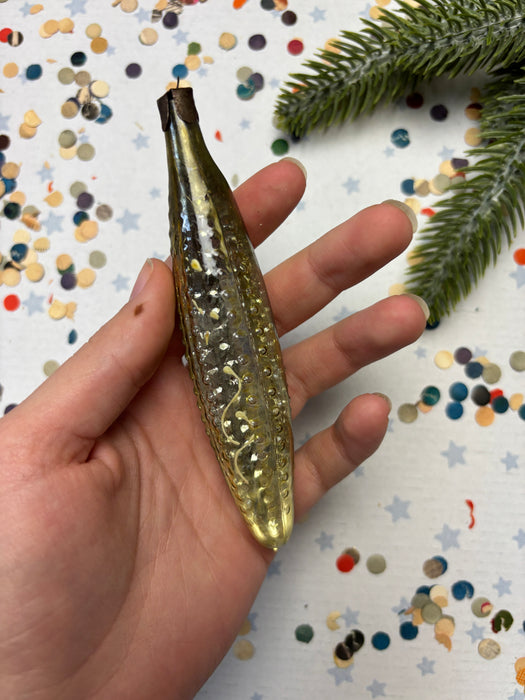 A hand holding a small, shiny, gold-colored object against a background of colorful confetti.