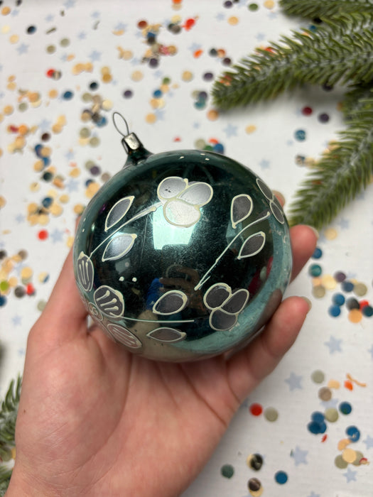 A hand holding a decorative ornament with a floral pattern against a background of colorful confetti.