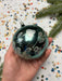 A hand holding a decorative ornament with a floral pattern against a background of colorful confetti.