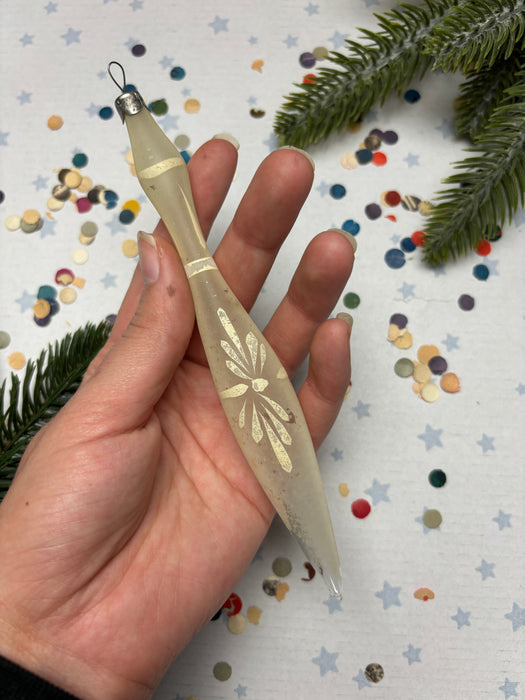 A hand holding a decorative object with a floral design, surrounded by colorful confetti and pine branches.
