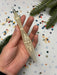A hand holding a decorative object with a floral design, surrounded by colorful confetti and pine branches.