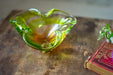 A green glass bowl with a curved shape sits on a wooden surface next to a red book with gold lettering.