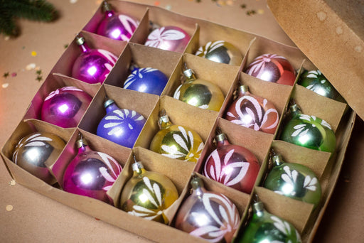 A cardboard box filled with colorful Christmas ornaments, including various shapes and sizes, arranged in rows.