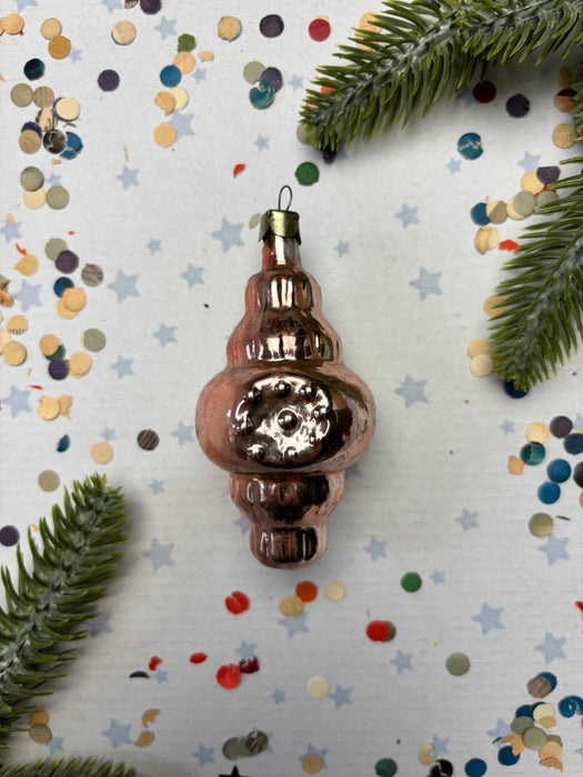 a shiny, metallic ornament with a reflective surface, surrounded by confetti and pine branches.