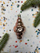 a shiny, metallic ornament with a reflective surface, surrounded by confetti and pine branches.