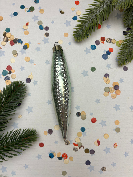 a shiny silver ornament with a pointed end, surrounded by colorful confetti and pine branches.