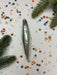 a shiny silver ornament with a pointed end, surrounded by colorful confetti and pine branches.