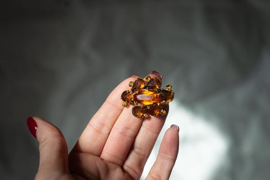 A hand holding a decorative piece of jewelry, possibly a brooch or pendant, against a blurred background.