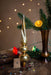 a golden Christmas ornament, a vase with greenery, and a number 2 sign on a wooden surface, all set against a backdrop of twinkling lights.