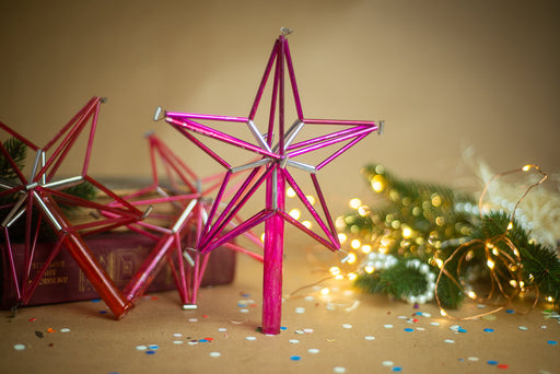 a pink star-shaped ornament, a Christmas tree, and some confetti on a table.