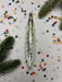 A silver ornament with a pointed end is placed on a background of colorful confetti and pine branches.