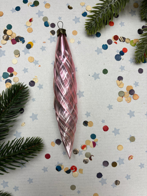 A pink spiral ornament is placed on a white background, surrounded by colorful confetti and pine branches.
