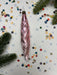 A pink spiral ornament is placed on a white background, surrounded by colorful confetti and pine branches.