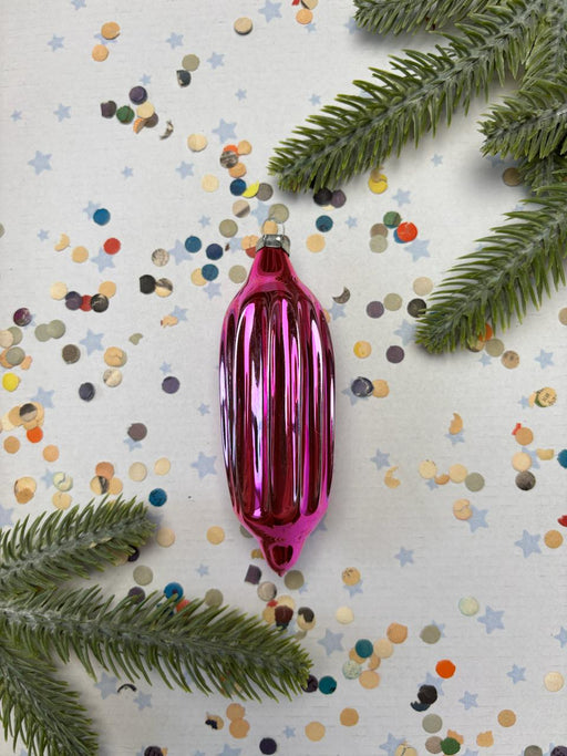 A pink Christmas ornament is surrounded by pine branches, confetti, and star-shaped decorations on a white background.
