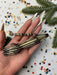 A hand holding a metal wire sculpture with a metallic bead attached, surrounded by confetti and pine branches.