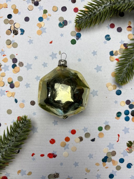a shiny, metallic ornament with a reflective surface, surrounded by colorful confetti and pine branches.